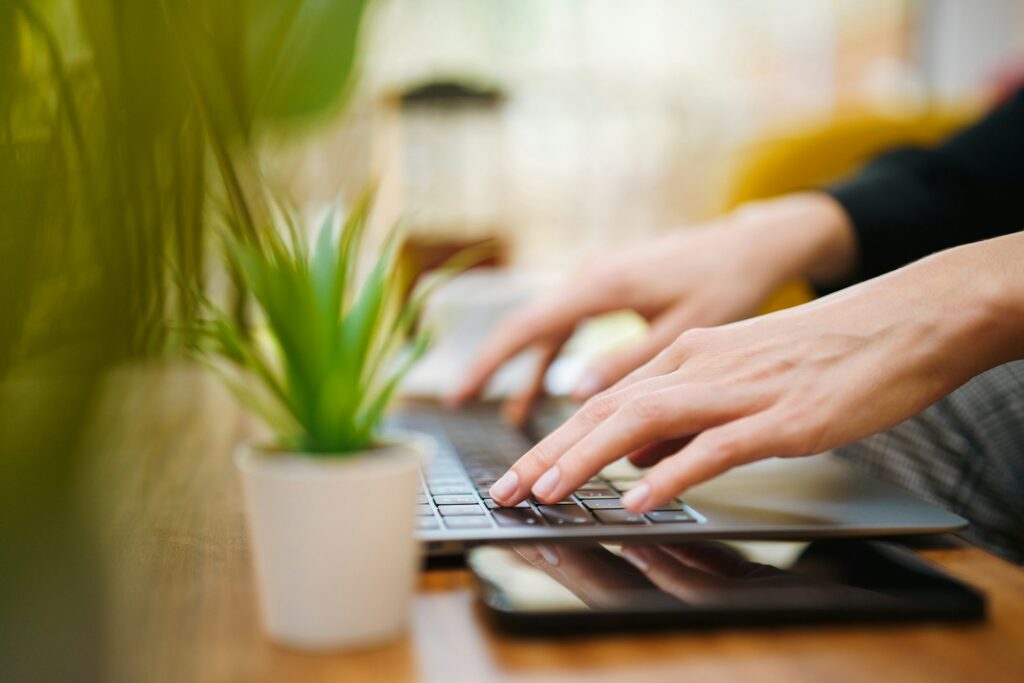 Typing on a laptop at a wooden table beside a plant